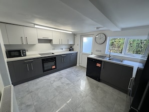 A modern kitchen with grey cabinets, a microwave, a dishwasher, and a clock on the wall. - Pet-friendly 3-bed house near Framlingham Castle, sleeps 5 (Framlingham)