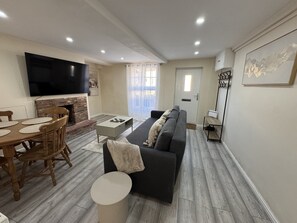 A living room with a flat-screen TV, a fireplace, a sofa, and a dining area with a wooden table and chairs. - Pet-friendly 3-bed house near Framlingham Castle, sleeps 5 (Framlingham)