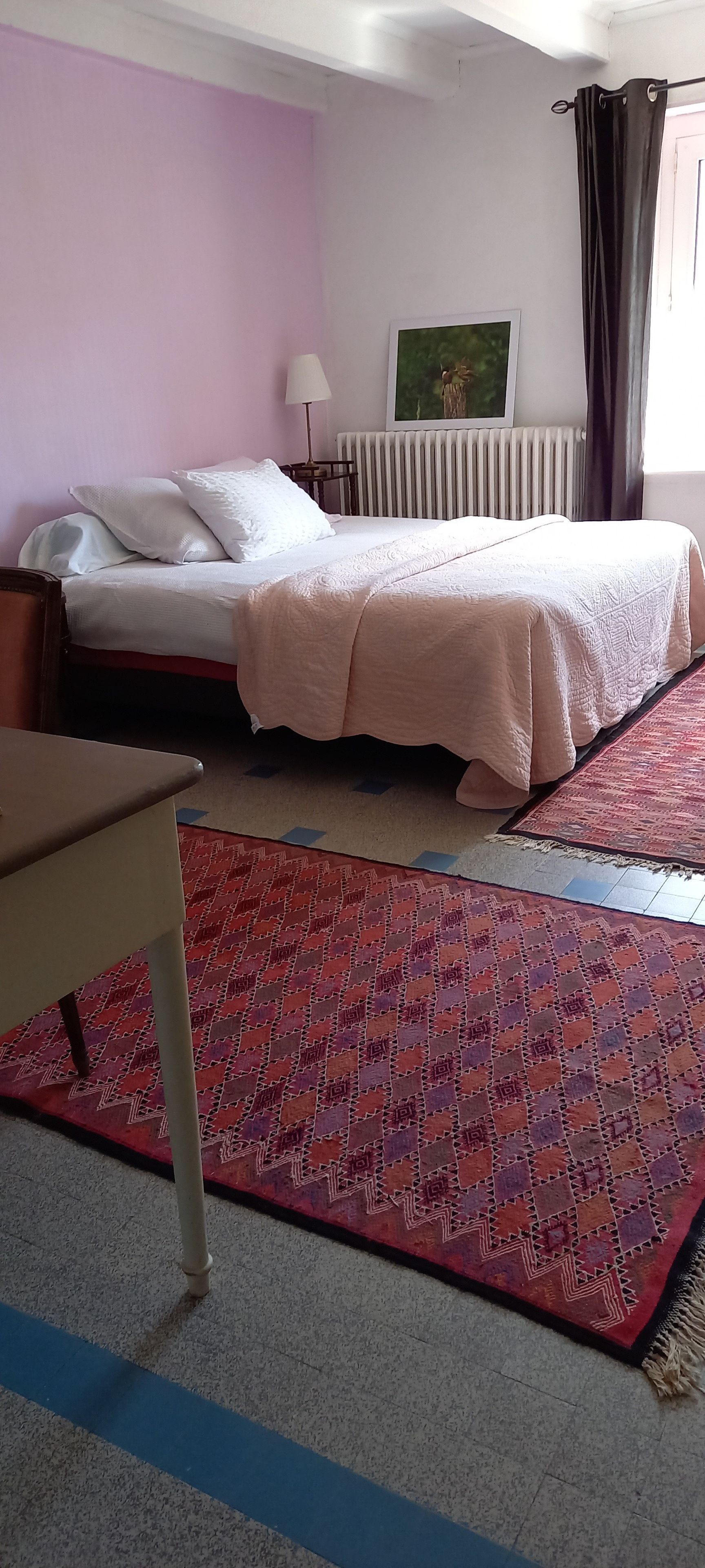 Een slaapkamer met een bed, een radiator, een lamp en een kamerbreed tapijt met een patroon.