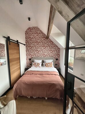 A bedroom with a sloped ceiling, a bed with a pink bedspread, two decorative pillows, and a wooden door. - Vrbo Property (Bullion)