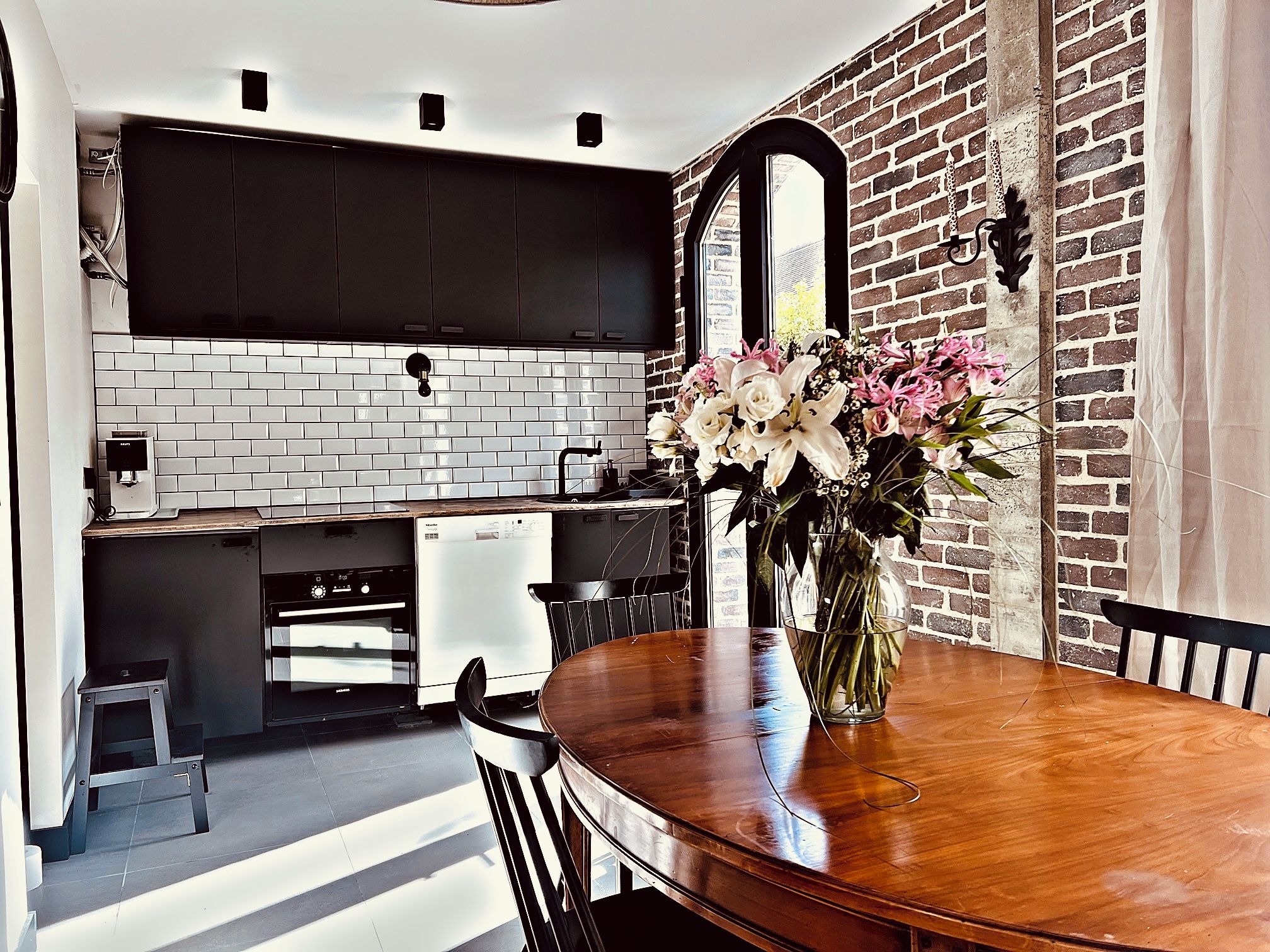 A modern kitchen with white subway tiles, a brick wall, and a dining area with a wooden table and chairs.