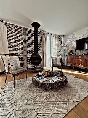 A cozy living room with a brick wall, a round wooden coffee table, a comfortable armchair, and a large flat-screen TV.