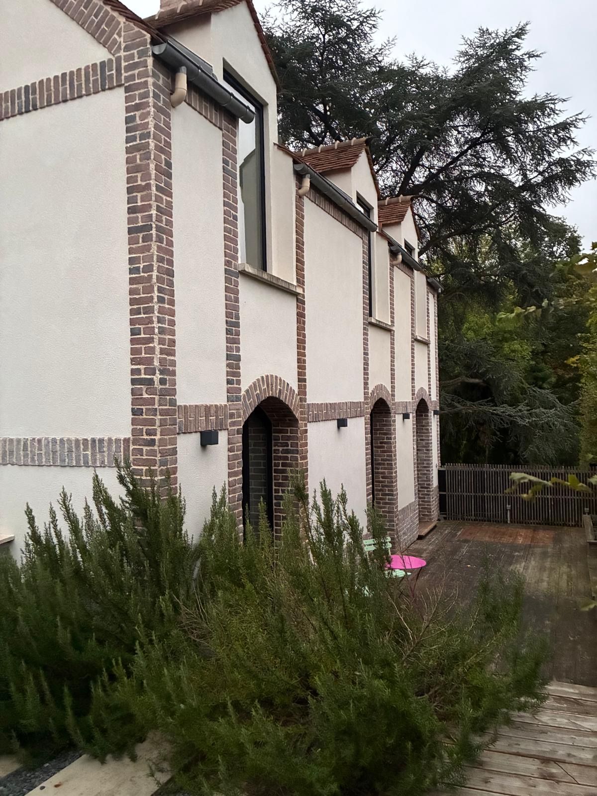 Un bâtiment à la façade blanche et aux éléments en brique brune, doté de nombreuses fenêtres et d’une porte bien visible.
