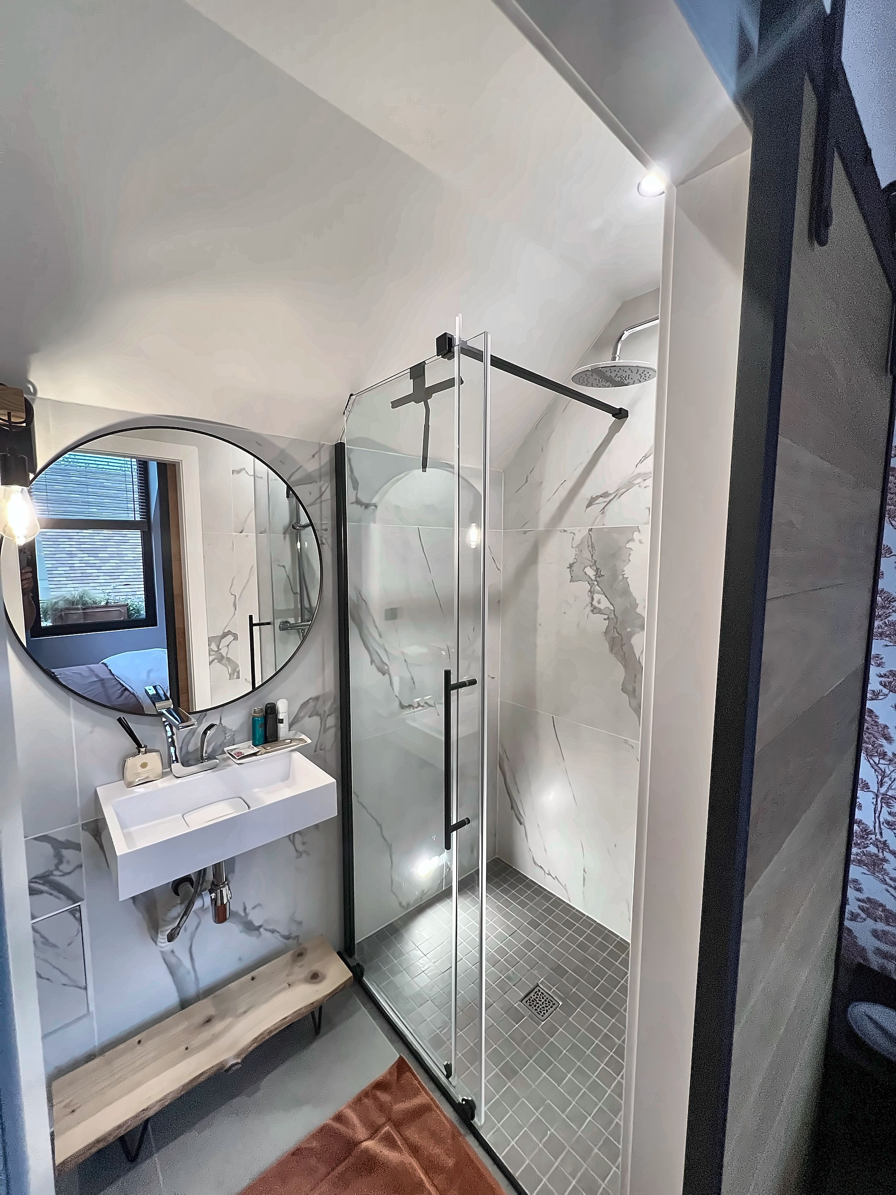 Une salle de bain moderne avec une douche à parois de verre, un miroir rond et un lavabo blanc.