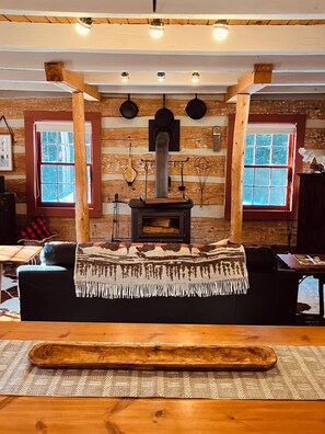 Ein gemütliches Blockhaus-Interieur mit einem zentralen Kaminofen, Holzwänden und einer Couch mit Decke.