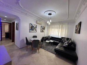 A modern living room with a black leather sofa, a round dining table with chairs, and abstract wall art. - Apparently, the Grand Hassan II Mosque is 2 minutes from the sea. (Dar-el-Beida)