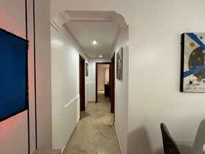 En hall med vita väggar, ett marmorgolv och en dörr längst ner som leder till ett annat rum.