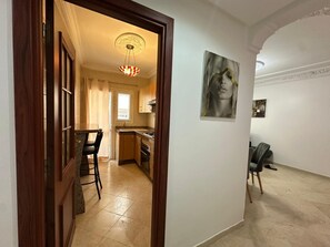 A hallway leading to a dining area with a table and chairs, a kitchen with cabinets and a stove, and a painting on the wall. - Apparently, the Grand Hassan II Mosque is 2 minutes from the sea. (Dar-el-Beida)