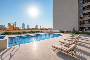 Ein Pool auf dem Dach mit Liegestühlen und einer Skyline im Hintergrund.