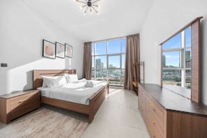 Ein modernes Schlafzimmer mit einem großen Bett, einem Nachttisch, einer Kommode und Blick auf die Stadt durch große Fenster.