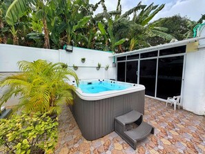 A hot tub in a covered outdoor area with stone flooring and potted plants.