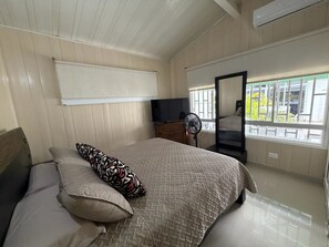 Ein Schlafzimmer mit Bett, Kommode, Fernseher und einem Fenster mit Blick auf Grünflächen.