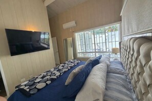 A bedroom with a bed, a mounted TV, a window with a view, and a ceiling fan.
