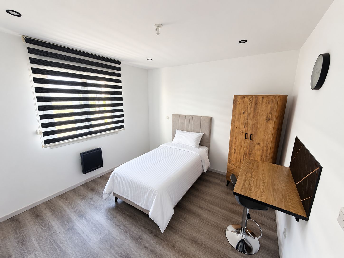 Ein modernes Schlafzimmer mit einem Bett, einem Holzschrank, einem Schreibtisch und einem Fenster mit Jalousien.