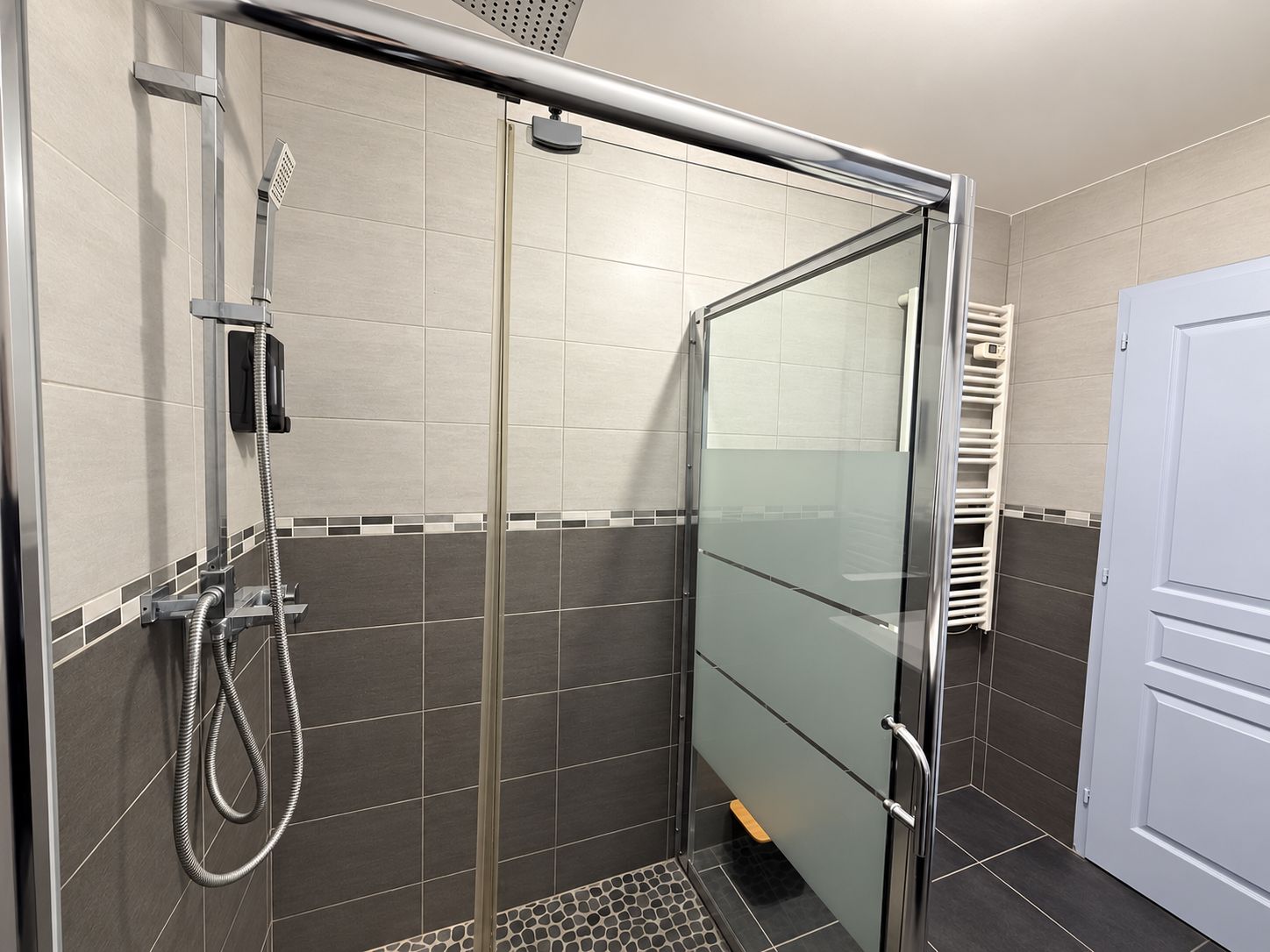 A shower area with a glass door, a handheld showerhead, and a towel rack.