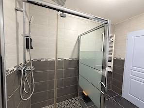 Un área de ducha con puerta de vidrio, un cabezal de ducha de mano y un perchero para toallas.