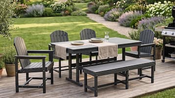Una terraza con mesa y sillas, rodeada por un jardín con diversas plantas.