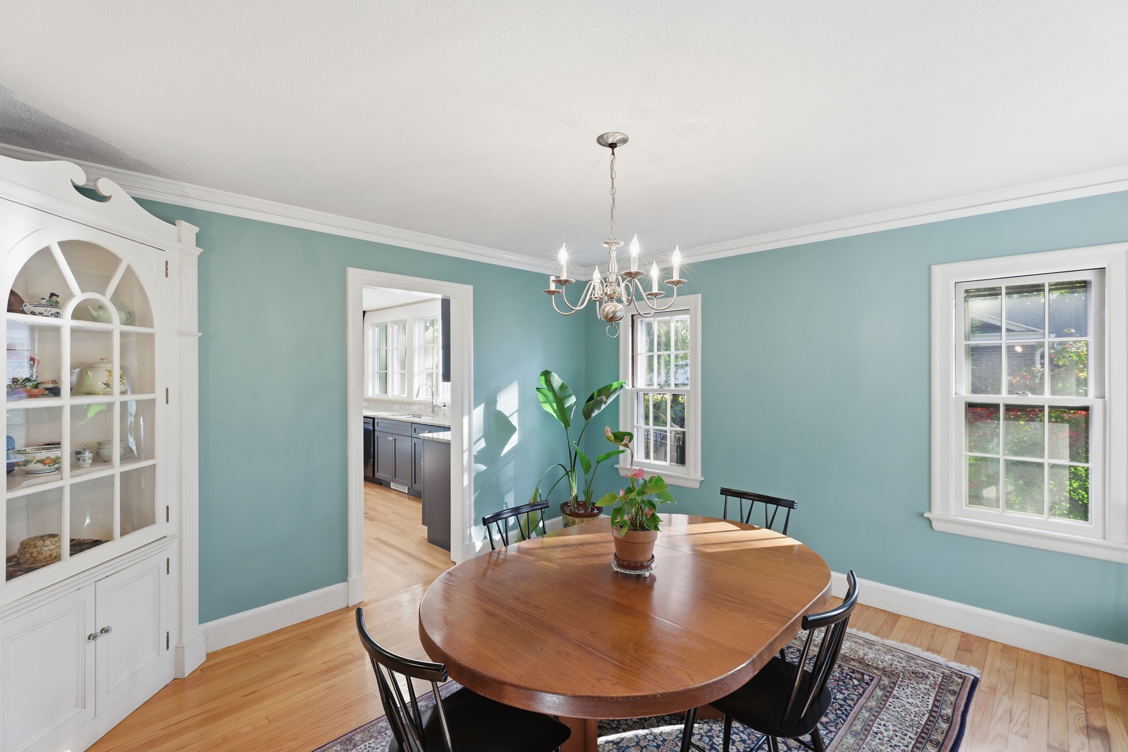 A dining room with a wooden table, chairs, a chandelier, and a potted plant.