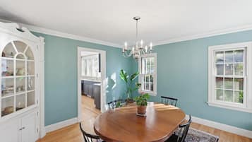 A dining room with a wooden table, chairs, a chandelier, and a potted plant.