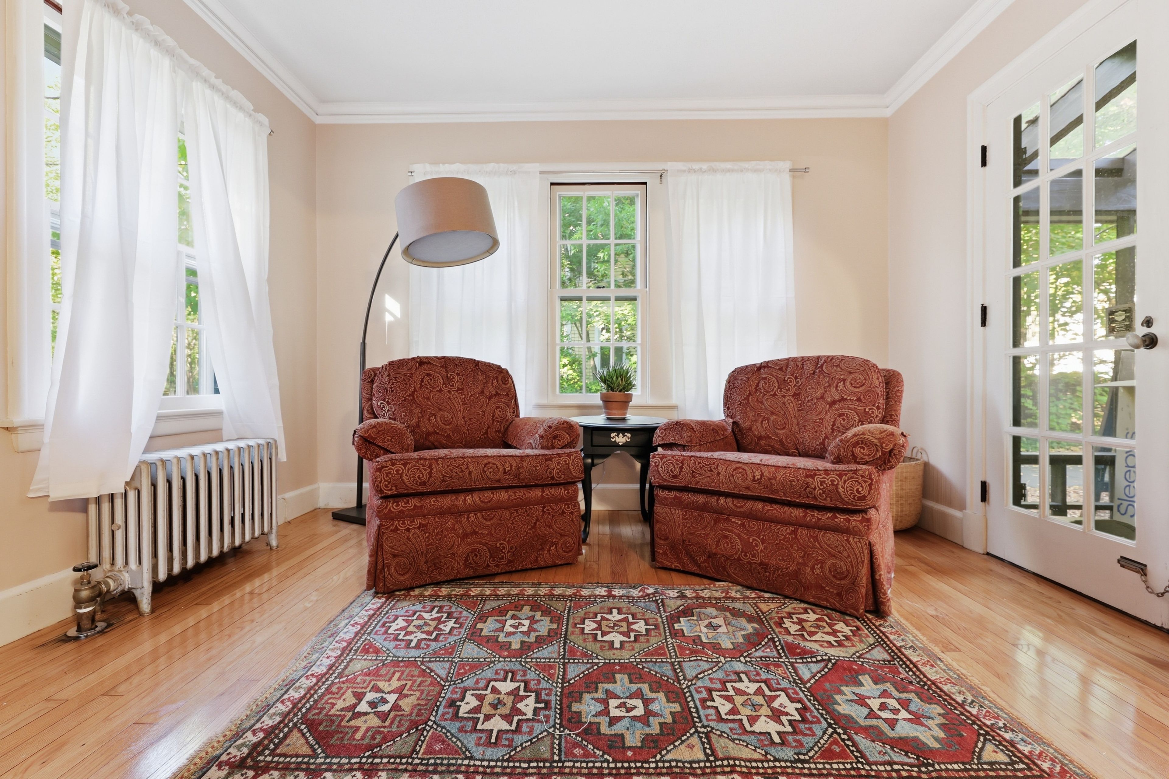 Ein Zimmer mit zwei Sesseln, einem gemusterten Teppich, einer Heizung und einer Tür mit Glasfeldern.