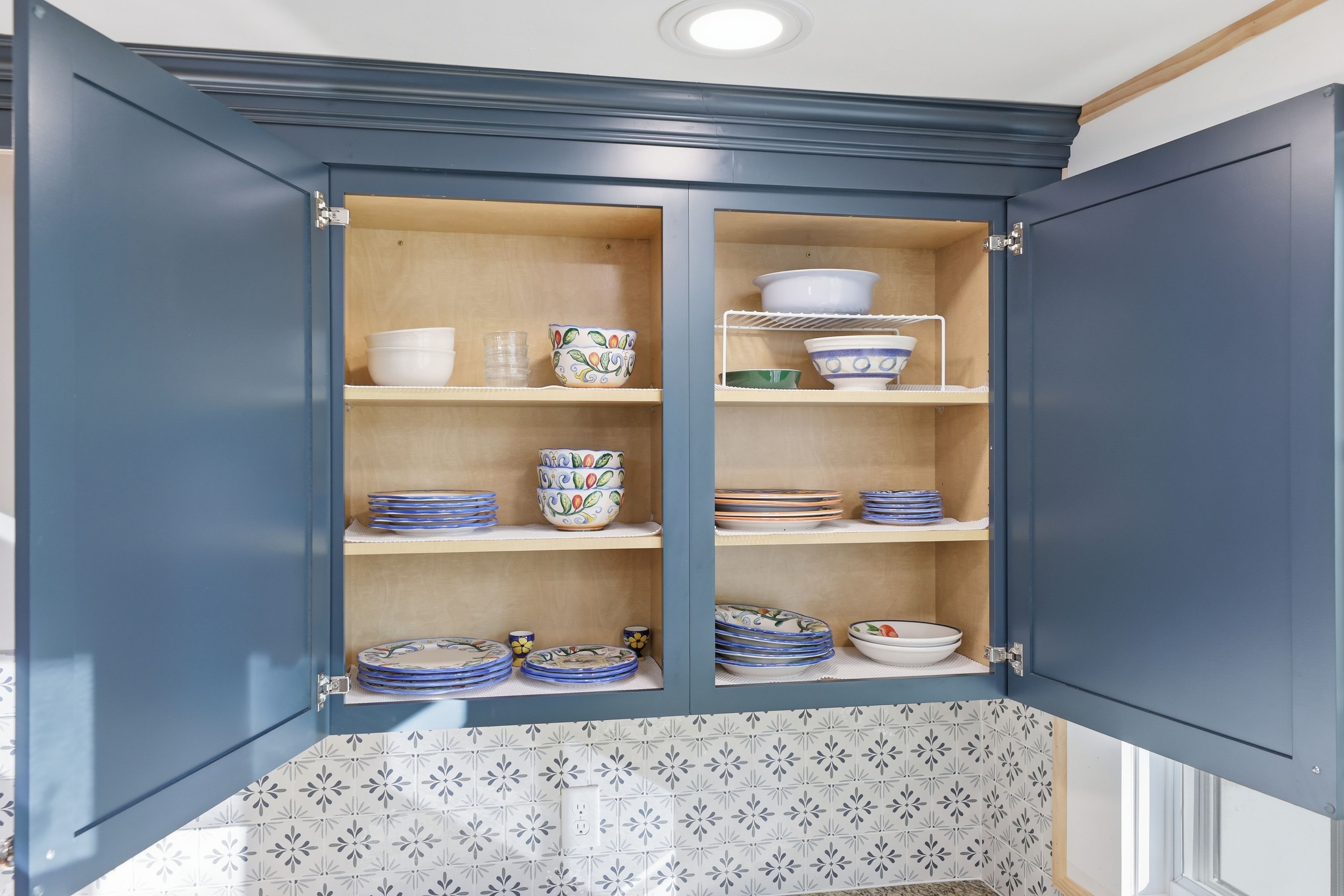 Een keukenkast met open deuren, waarbinnen borden en ander servies op planken staan, en een klein plankje met een kom.