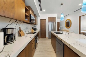A modern kitchen with wooden cabinets, a marble countertop, a built-in oven, and a stainless steel refrigerator. - 2BR Beachfront Condo With Pool Access & Terrace ! (San José del Cabo)