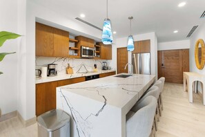 A modern kitchen with a central island, wooden cabinets, stainless steel appliances, and pendant lighting. - 2BR Beachfront Condo With Pool Access & Terrace ! (San José del Cabo)