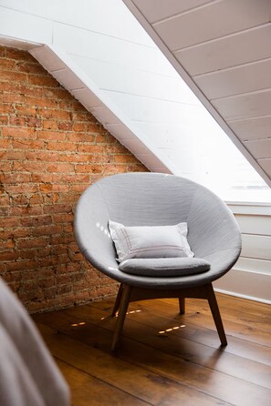 A chair with a cushion in a room with a sloped ceiling and a brick wall. - The Sycamore Downtown Modern Home (Lancaster)