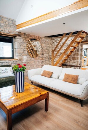 A modern living room with a stone wall, a white sofa, a wooden coffee table, and a wooden staircase. - Exceptional thatched cottage, Nordic bath, and wood-burning fire (Ploemeur)