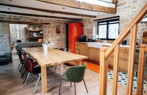 A rustic kitchen with a wooden table and chairs, a red refrigerator, and stone walls. - Exceptional thatched cottage, Nordic bath, and wood-burning fire (Ploemeur)