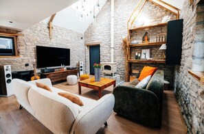 A cozy living room with a stone wall, a flat-screen TV, a fireplace, and comfortable seating. - Exceptional thatched cottage, Nordic bath, and wood-burning fire (Ploemeur)