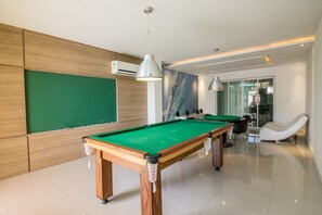 Ein Billardtisch in einem modernen Raum mit grüner Spieloberfläche, einer weißen Deckenleuchte und einem großen Fenster im Hintergrund.