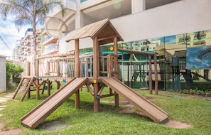 A playground with wooden slides and climbing structures, set against a backdrop of modern buildings and a clear sky. - Luxury Beachfront Apartment in Arraial do Cabo – Sea Views, Pools & BBQ (Cabo Frio)