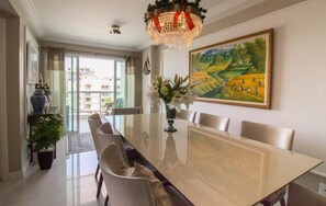 A dining area with a long table, chairs, a chandelier, and a painting on the wall. - Luxury Beachfront Apartment in Arraial do Cabo – Sea Views, Pools & BBQ (Cabo Frio)