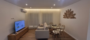 A modern living room with a flat-screen TV, a sofa, a dining table with chairs, and a decorative wall piece. - Ondas Beach House
Designed for your natural living a few steps from the beach (Monte Gordo)