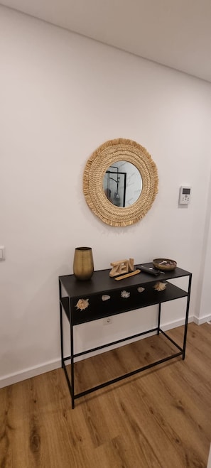 A room with a round woven mirror on the wall, a black metal console table with decorative items, and a wooden floor. - Ondas Beach House
Designed for your natural living a few steps from the beach (Monte Gordo)