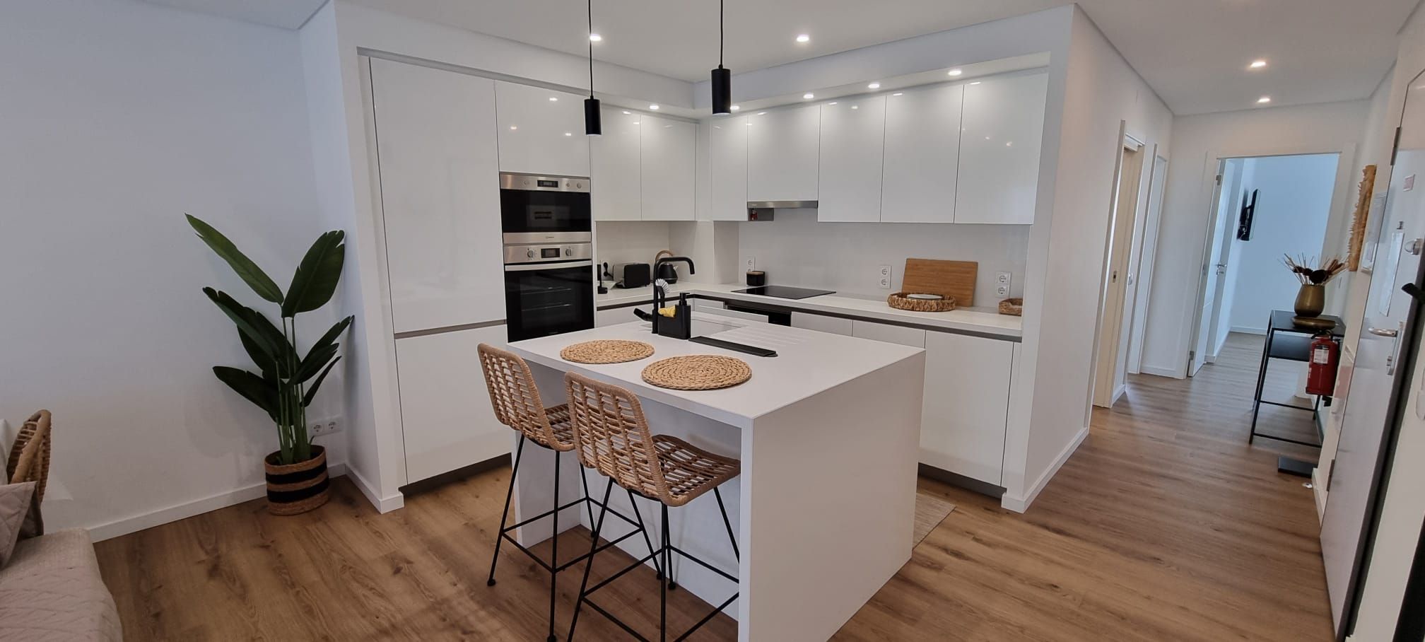 Una cocina moderna con armarios blancos, una isla central con taburetes altos y una planta en maceta.