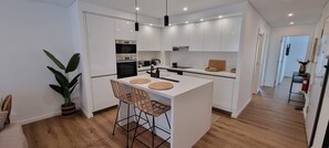 A modern kitchen with white cabinetry, a central island with bar stools, and a potted plant. - Ondas Beach House
Designed for your natural living a few steps from the beach (Monte Gordo)