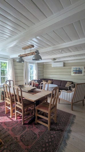 A dining area with a wooden table and chairs, a patterned rug, and a ceiling with exposed beams.