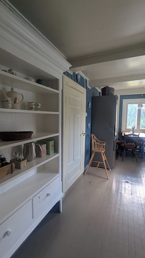 A room with a white cabinet with shelves, a wooden chair, and a table with chairs.