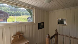 Et værelse med et vindue der kigger ud over et grønt landskab, en træbænk og et billede i ramme på væggen.