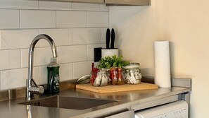 A kitchen with a stainless steel sink, a dish soap bottle, a cutting board with jars, a paper towel holder, and a knife block. - Stylish 1-Bed Apartment in the heart of Manchester (Unknown)