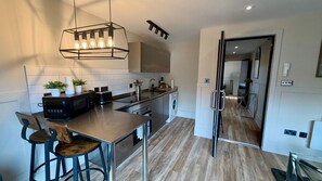 A modern kitchen with a central island, a dining area with a bar stool, and a visible hallway leading to another room. - Stylish 1-Bed Apartment in the heart of Manchester (Unknown)