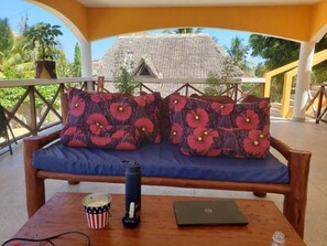Een balkon met een houten bankje, een laptop, een tumbler en een emmer popcorn.