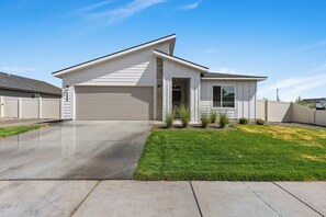 A single-story house with a garage, a well-maintained lawn, and a clear sky. - Warm Modern 4BR Retreat. Pets Welcome. Fenced Yard. Near I-84 (Nampa)