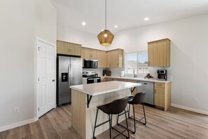 A modern kitchen with a central island, stainless steel appliances, and wooden cabinetry. - Warm Modern 4BR Retreat. Pets Welcome. Fenced Yard. Near I-84 (Nampa)
