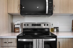 A kitchen with a black microwave, stainless steel oven, and a knife block. - Warm Modern 4BR Retreat. Pets Welcome. Fenced Yard. Near I-84 (Nampa)