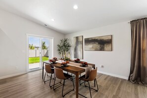 A dining area with a wooden table, chairs, and a view of a backyard. - Warm Modern 4BR Retreat. Pets Welcome. Fenced Yard. Near I-84 (Nampa)
