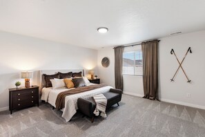 A bedroom with a bed, nightstands, a lamp, a clock, and a window with curtains. - Warm Modern 4BR Retreat. Pets Welcome. Fenced Yard. Near I-84 (Nampa)