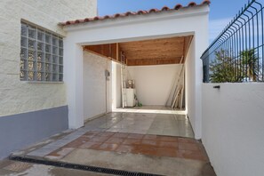 Un couloir étroit, dont le sol est recouvert de carreaux, mène à une zone abritée avec un plafond en bois.